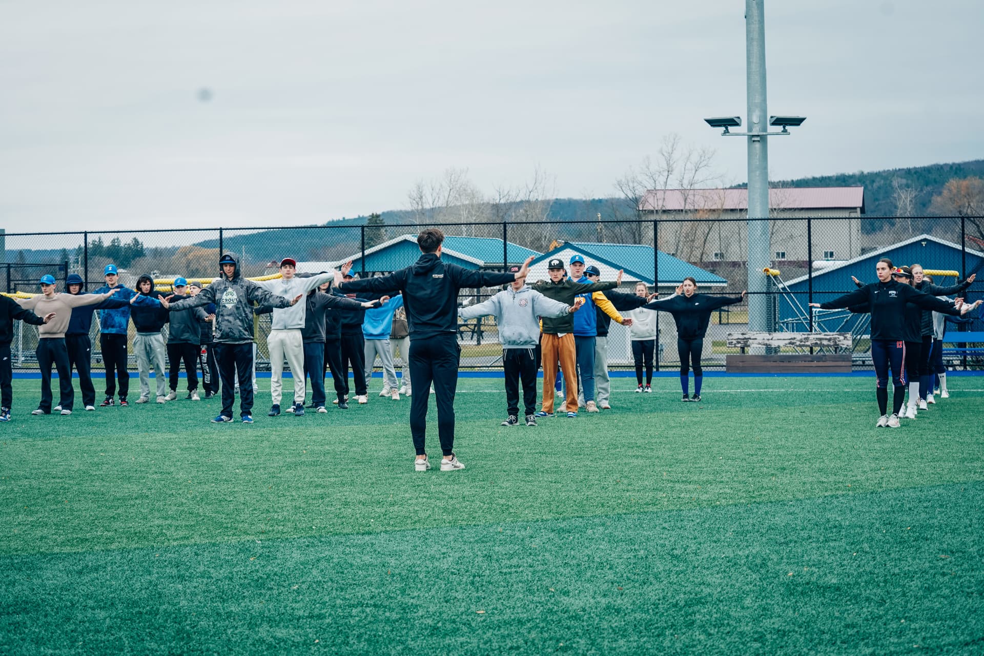 Coach leading a youth sports team through a warm-up on the turf field